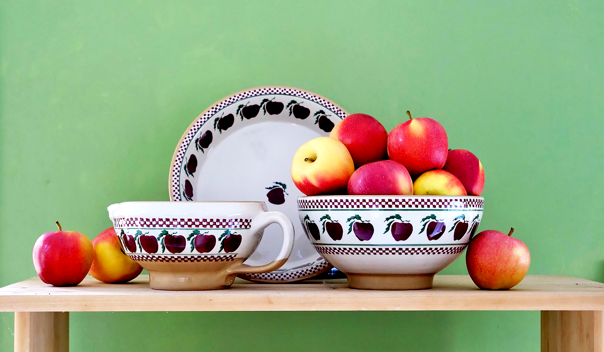 Nicholas Mosse Pottery Classic Pie Dish, Batter Bowl and Large Bowl in Apple Pattern against a green background with red apples for Autumn